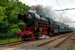 Vintage steam train passing through lush greenery in Baarn, Utrecht, Netherlands.
